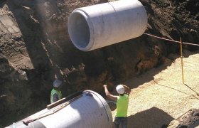 Excavator being used to lower a large section of concrete piping