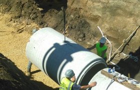 Excavator being used to lower a large section of concrete piping